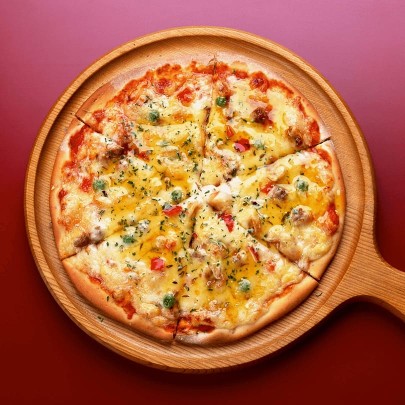 A freshly baked Little Villa's Pizza, topped with cheese, herbs, and vegetables, on a wooden serving board.