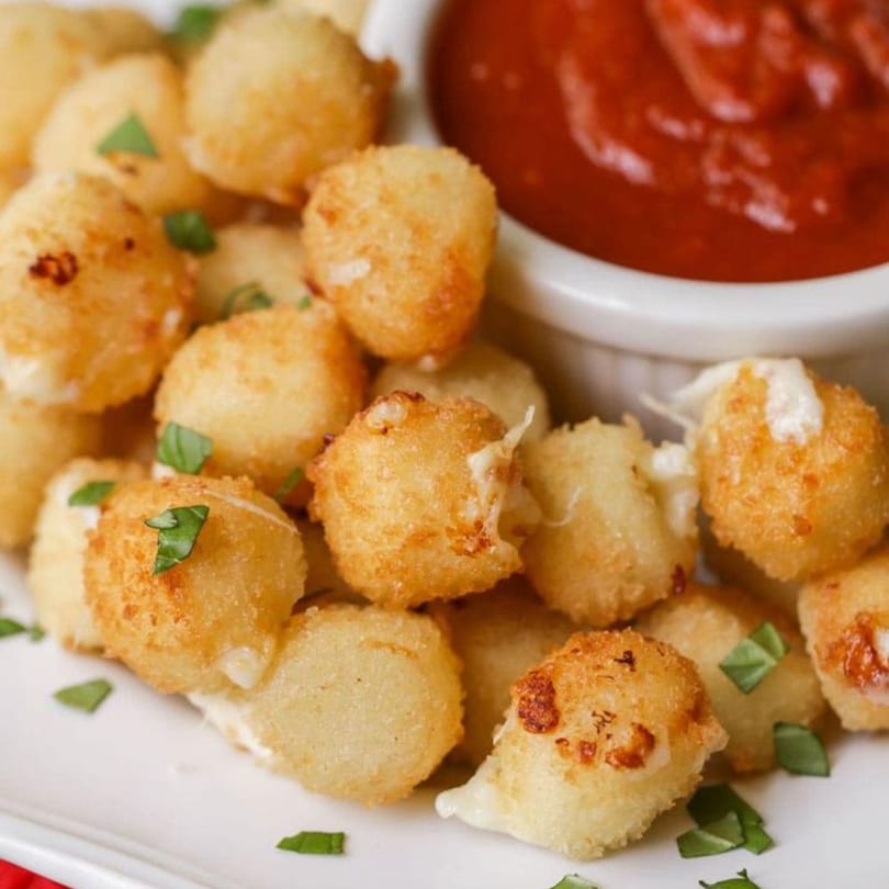 Golden-brown fried mozzarella balls with fresh basil and a side of red marinara sauce.