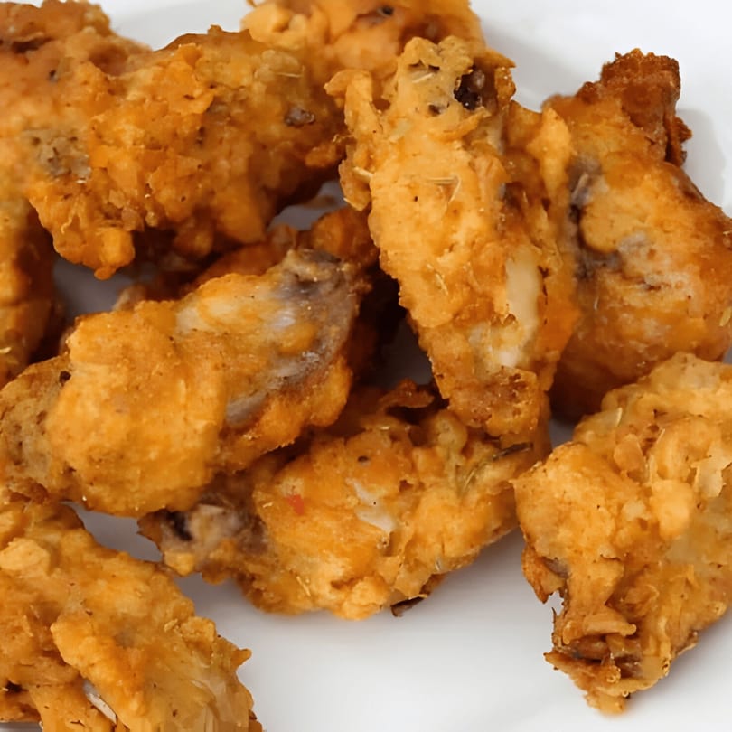 Close-up of golden-brown fried chicken wings, crispy and seasoned, on a white plate.